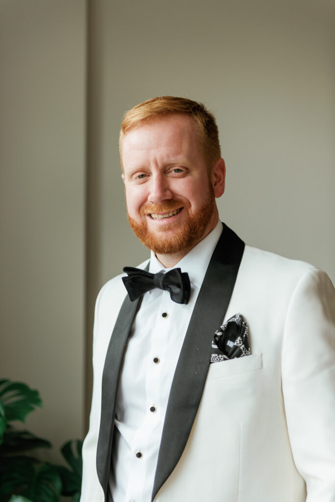 Groom portrait in a white dinner jacket smiling before the ceremony.