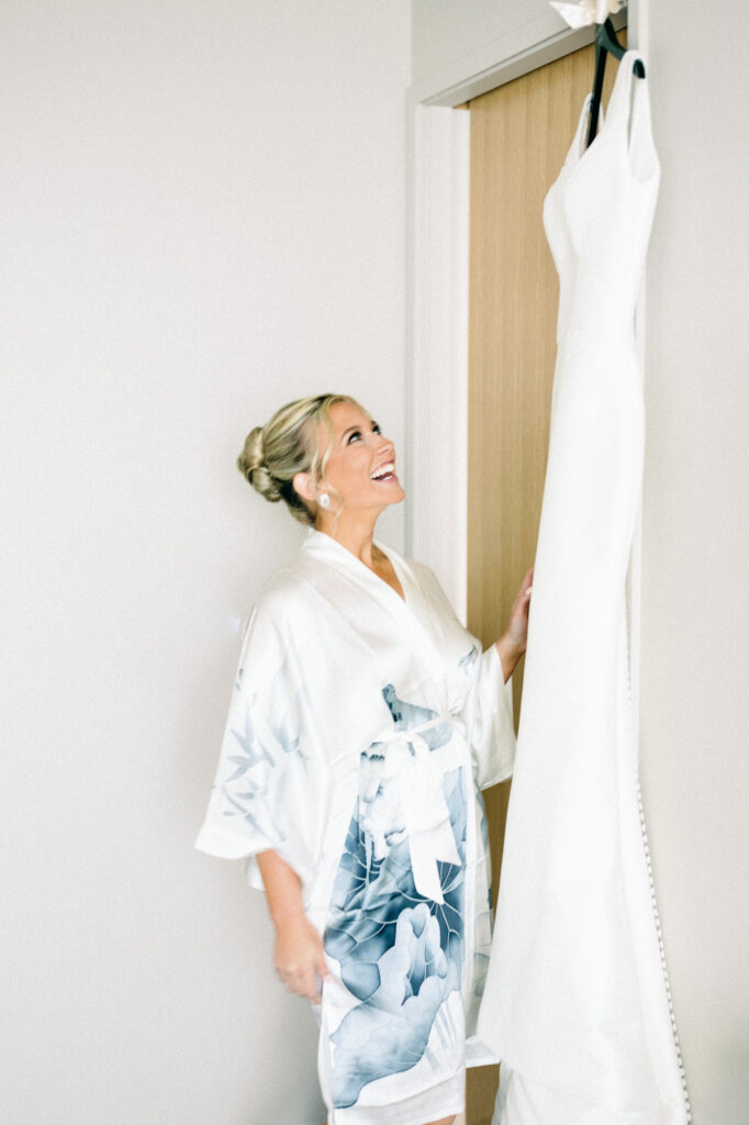 Bride getting ready and looking at her wedding dress hanging in the hotel suite.