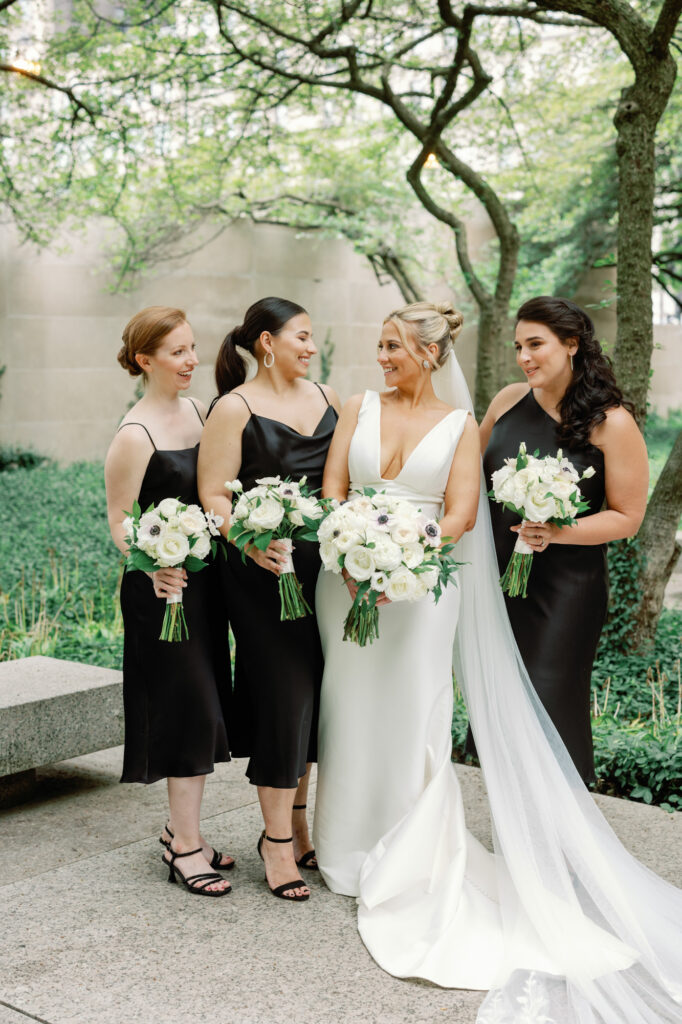Bridesmaids in black dresses holding bouquets during wedding portraits at the Art Institute of Chicago Gardens.