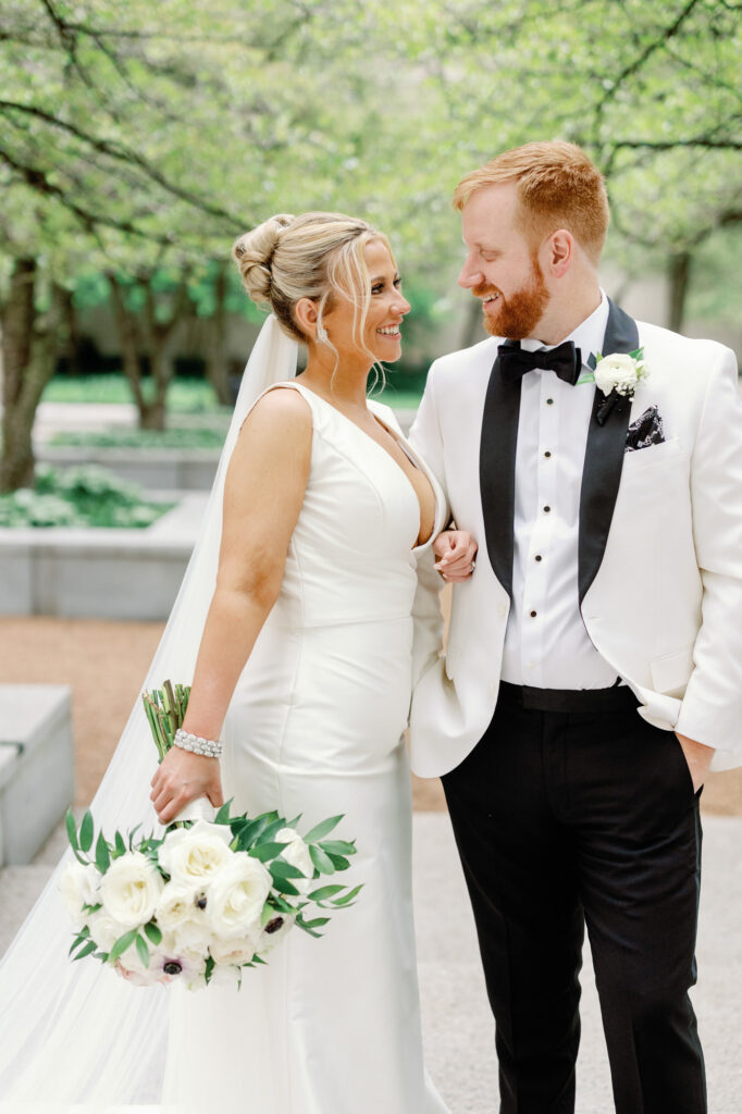 Bride and groom smiling at each other while walking through the Art Institute Gardens.