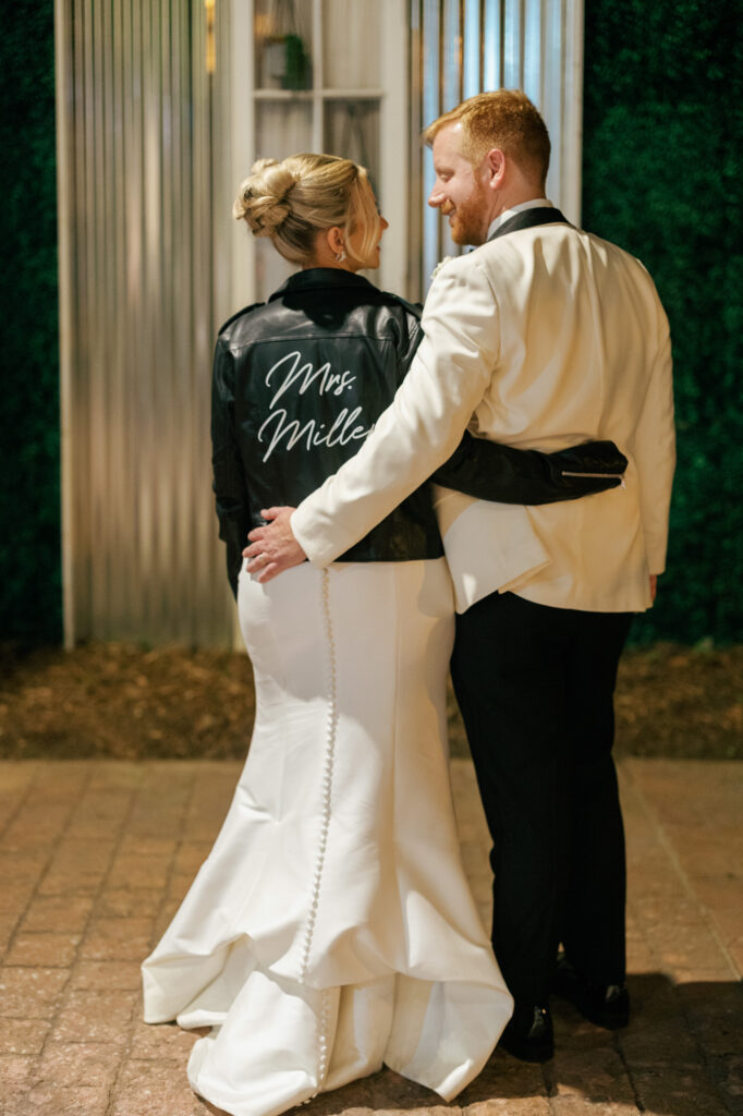Bride wearing a custom jacket embracing the groom at the end of the night.
