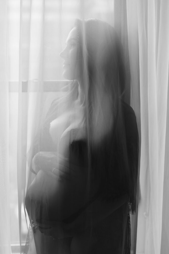 Artistic maternity photos through sheer curtains with soft blurred silhouette