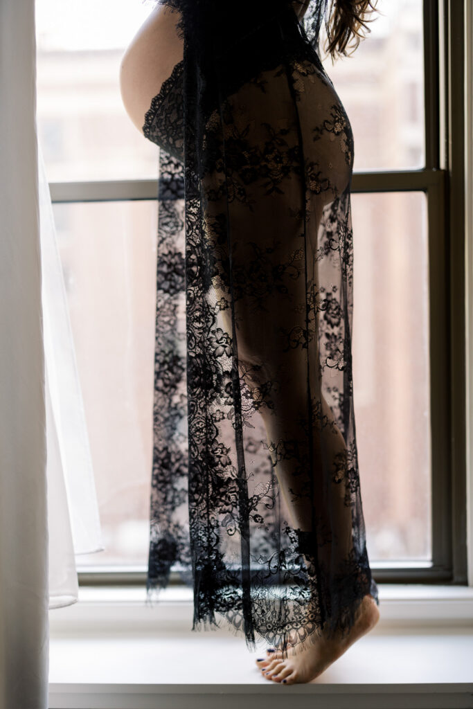 Bare feet of pregnant woman standing on window ledge with lace robe