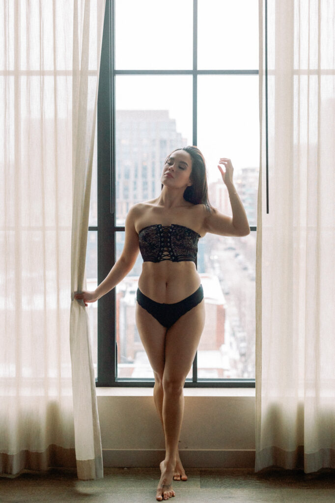 Boudoir portrait of woman standing by floor to ceiling windows in Chicago hotel room