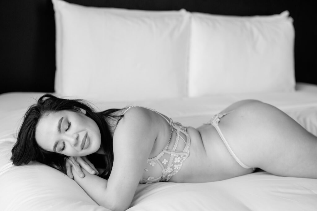 Black and white boudoir photo of woman lying on bed in delicate lingerie