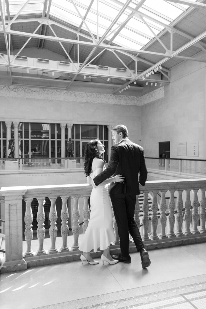 Black and white museum engagement photo couple embracing by railing