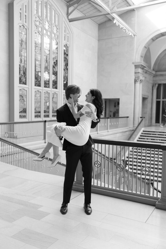 Black and white engagement photo groom lifting bride inside Art Institute Chicago