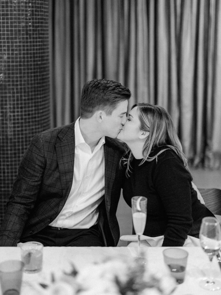 Black and white photo of couple kissing at table during dinner