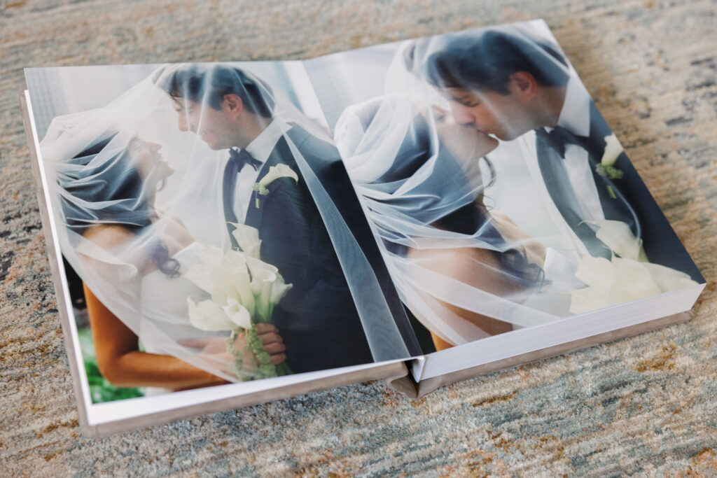 Vertical wedding album spread featuring bride and groom portraits through veil in soft light